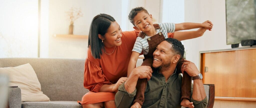 Laughing toddler sitting on dad's shoulders as parents smile at each other