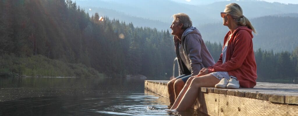 Mature couple sitting on dock and dipping feet into water at the cottage