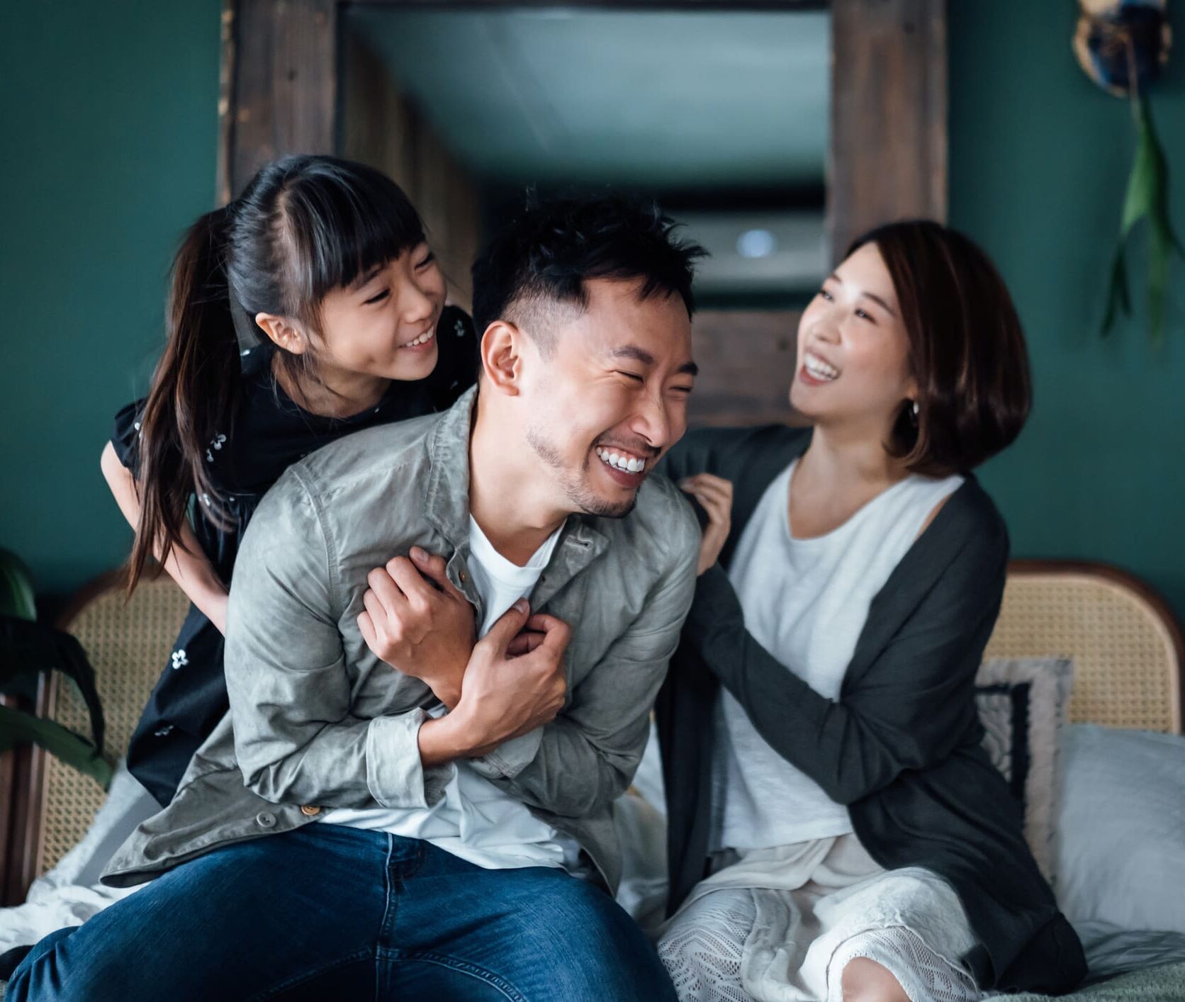 Playful young Asian family having fun playing at home while mother and daughter tickling father in bed. Family life with love and happiness