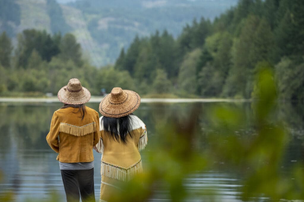 Back view of two Indigenous women staring out at lake view together